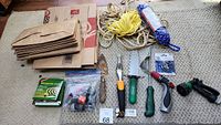 Overview of garden tools, hose accessories, twine, mosquito coils, and brown paper bags displayed on floor