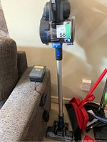 Photo showing full Hoover ONEPWR cordless stick vacuum standing upright next to sofa, with battery charger placed on sofa armrest.