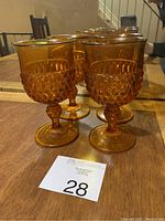 Photo showing four amber water goblets with Diamond Point pattern by Indiana Glass, displaying bowl and stem details.