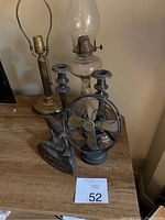 Overall view of the metal decor items on a wooden surface, featuring the fan, flat iron, candle holders, and oil lamp.