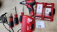 Full view of Milwaukee cordless drill, three screwdrivers, and battery charger on carpeted floor.