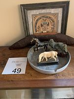Three horse figurines displayed on a marble ashtray with framed sandpainting and wood boomerang behind