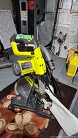 Side view of the Ryobi miter saw showing the yellow handle, base, and dust collection bag.