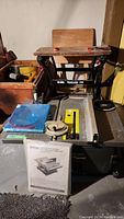 Full view of Ryobi Workmaster 200 table saw with yellow throat plate and accessories including operator's manual and blue plastic piece on table.