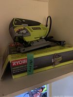 Photo of Ryobi green and black variable speed jigsaw on top of its original box.