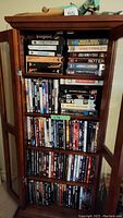 Full view of wooden cabinet with glass doors filled with DVDs and VHS tapes on shelves.