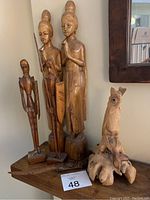 Four carved wood sculptures on corner table including three standing human figures and one owl on wood base.