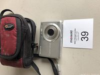 Sony Cyber-shot digital camera front view showing lens and power button beside a Lowepro carrying case