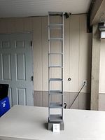 Tall vertical metal CD holder rack with eight shelves displayed on a table against a wall.