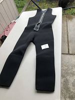 Full view of the black dry suit laid flat showing sleeveless design and legs with a large zipper on front.