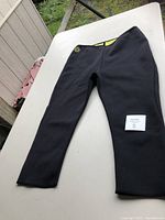 Front view of black dry suit pants with yellow interior, laid flat on a table.