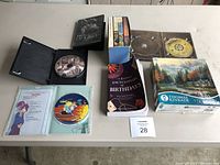 Photo showing DVDs including Les Miserables, an animated DVD, multiple smaller books in a box, Encyclopedia of Birthdays book, and Thomas Kinkade puzzle box
