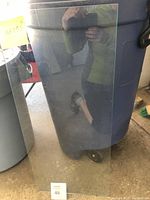 Full view of rectangular glass sheet leaning against a trash bin in a garage or storage area.