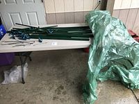Green plastic or metal connectors with green metal frame poles and metal hooks laid in a heap on a table.