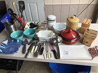 Overview of kitchen supplies lot on table showing bowls, utensils, cookware, and storage jars.