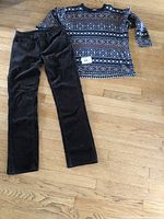 Photo of ladies' sweater with patterned design and dark corduroy pants laid on wooden floor