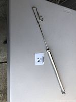 Full view of the metal slide whistle on a white table showing the looped handle and straight body