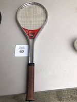 Full view of racquetball racket showing metal frame, brown grip, and stringed hitting surface.