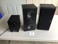 Overall photo showing the powered subwoofer and two bookshelf speakers, one with grille and one without.