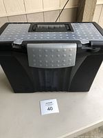 Front view of the closed black plastic storage box featuring a textured lid with gray latch and built-in handle.