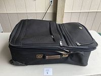 Full side view of soft black suitcase showing zippered compartments and side handle.