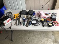 Overview of assorted hand and measuring tools laid out on a white folding table in a garage setting.