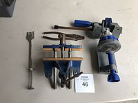 Four clamping and pressing tools arranged on flat surface: two with wooden components, two with metal and blue handles