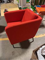 Side view of one red IKEA Ekero armchair showing fabric upholstery and metal legs.