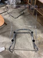 Close-up of one transparent acrylic chair with chrome cantilever base showing scuffs and clear seat profile.