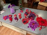 Multiple Danbury Mint Red Hat Society Christmas ornaments laid out on counter including figurines and decorative feathered hats in red and purple.