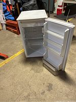 Full view of the small upright refrigerator with door open showing three door shelves and two wire shelves inside fridge compartment.