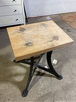 Front angled view of butcher block tabletop showing natural wood with knots and wear marks and sturdy iron base with curved legs.