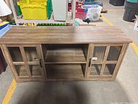 Front view of the wood TV stand with two glass paneled cabinet doors and central open shelving section.