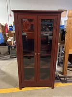 Front view of a wood cabinet with glass double doors closed, showing the full height and structure.