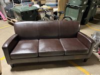 Front view of a brown leather couch with three seat cushions and a low backrest, highlighting the overall shape and condition.