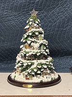 Full view of ceramic Christmas tree decorated as a snowy village scene with houses, people, horse sleigh and snow accents on a wooden base.