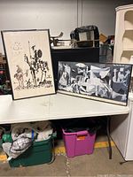 Two framed Picasso prints displayed on a table, including the Don Quixote lithograph on the left and the Guernica print on the right.