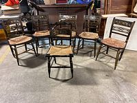Overview photo of all six vintage wood dining chairs showing painted black frames with gold accent lines, floral painted backrests on five chairs, and woven rush seats.