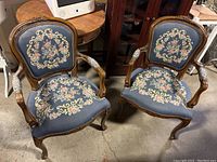 Pair of vintage wooden upholstered living room chairs with blue fabric and floral embroidery, carved wood frames, and beaded trim.