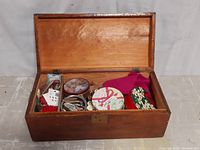 Large wooden sewing box open showing assorted sewing materials inside including containers with thread, needles, buttons, and fabric pieces.