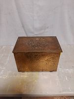 Full front view of the embossed brass kindling fireplace box showing the hammered texture and embossed tavern scene on the lid.