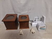 Two wooden square canisters with flip lids and round glass windows on top, one larger and one smaller, placed side by side with two turtle-shaped salt and pepper shakers in front and a white spiralizer with attachments behind them.