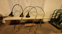 Three porcelain commercial lights with curved metal arms shown standing side by side in a workshop space.