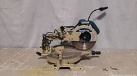 Side-front view of Makita sliding compound miter saw set on a table showing full saw, base, handle, and blade guard.