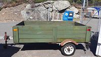 Left side view showing green-painted wooden sideboards, steel frame, hitch coupler and side reflector lights.