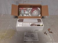 Opened box showing small ceiling fan components inside; includes white fan blades, parts in plastic, and instruction manual.