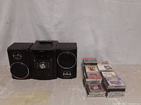 Black Sharp stereo receiver with central unit and two detachable speakers, remote control on top, next to stacks of compact disks.