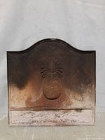 Front view of vintage cast iron sign showing embossed pineapple and surface rust.