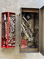 Top-down view inside metal toolbox showing socket set in red tray alongside various wrenches and ratchets in the base.