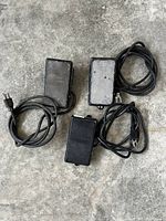 Top view of three black foot pedal switches placed on concrete floor showing power cords and plugs.